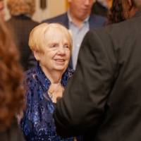 Woman attending reception wearing a sparkly blue shirt, speaking with other guest